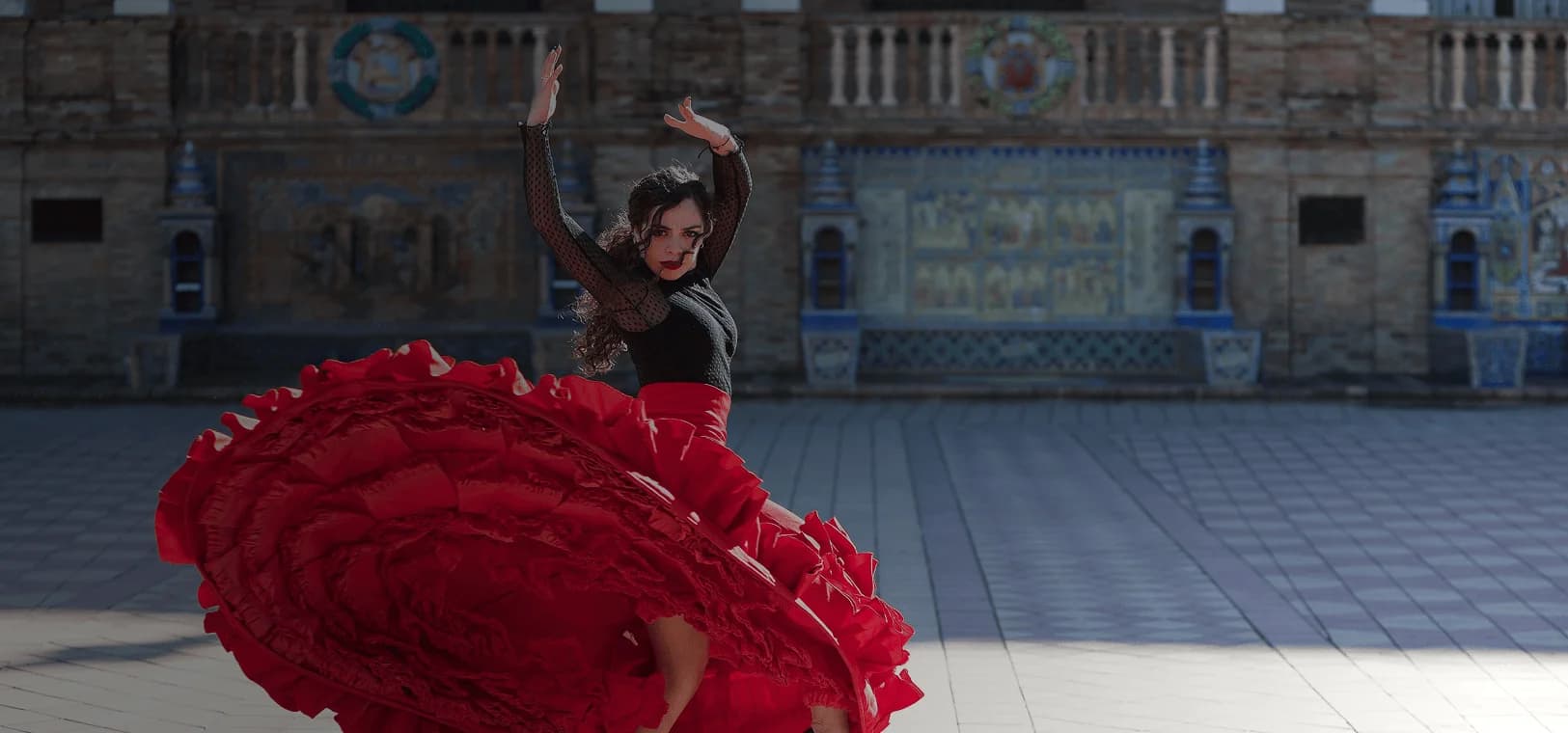 Flamenco dancer spins in front of majestic building backdrop. Overlaid is the Spanish word “bailar” with its English translation, "to dance".