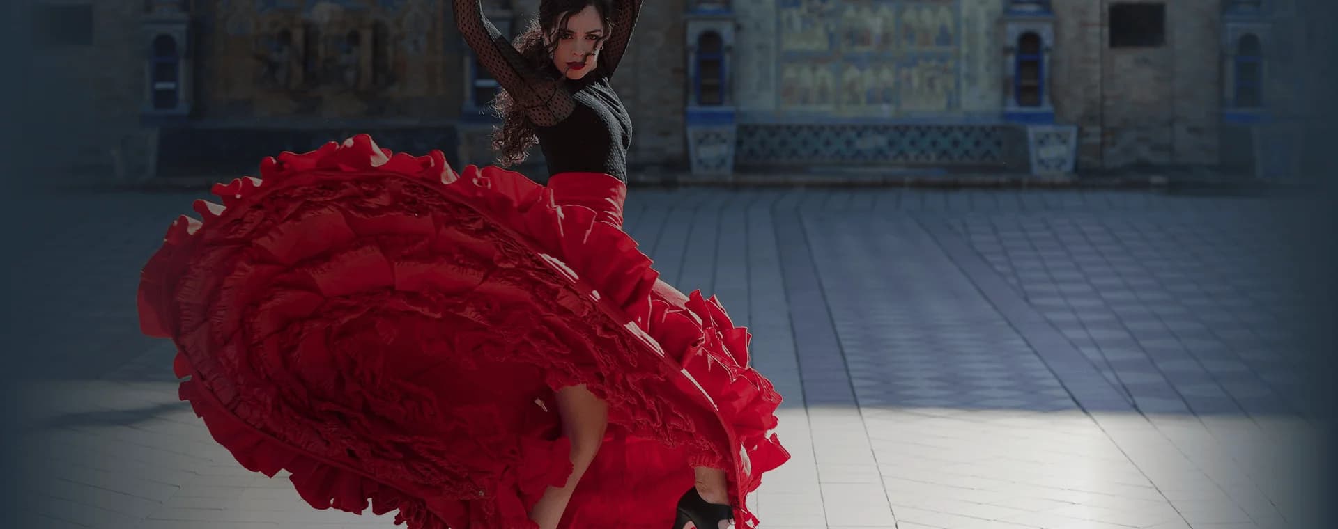 Flamenco dancer spins in front of majestic building backdrop. Overlaid is the Spanish word “bailar” with its English translation, "to dance".