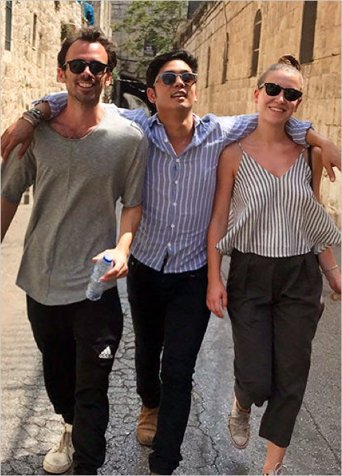 Three young, smiling friends walk down a European road.